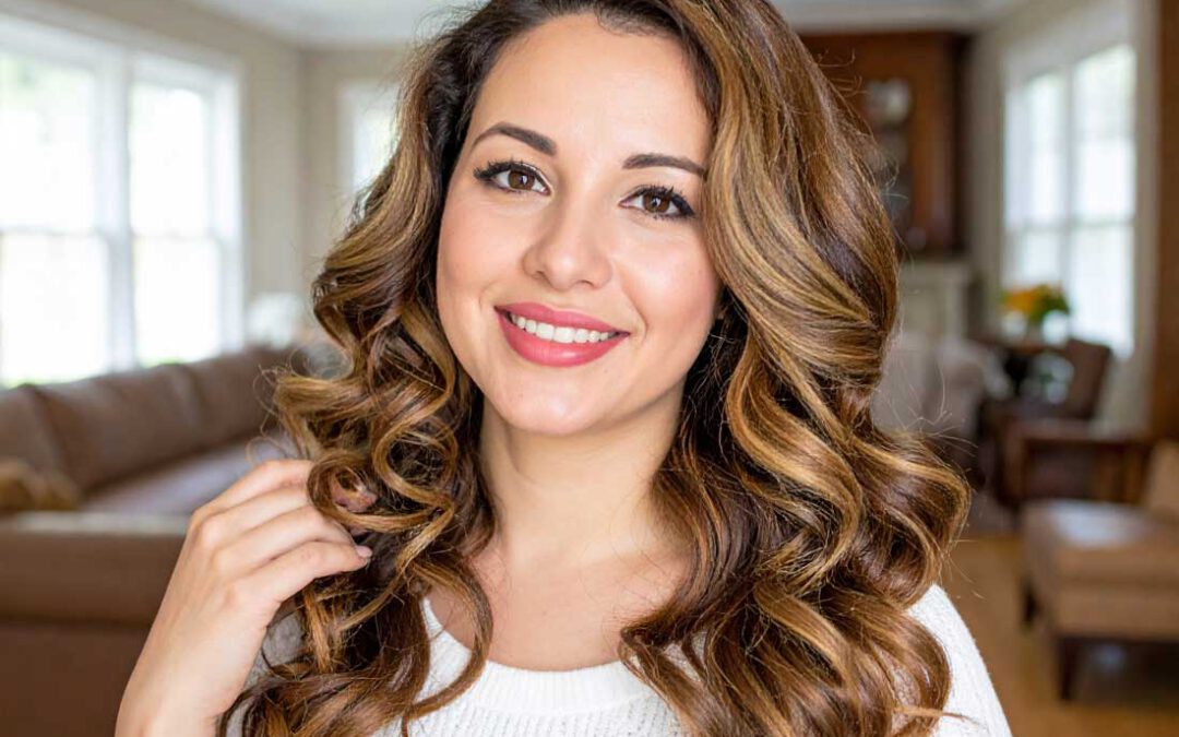 Frau mit langem, gelockten Echthaar in Braun mit Highlights, gestylt mit Bonding-Extensions – Frisur-Inspiration im Wohnzimmerambiente