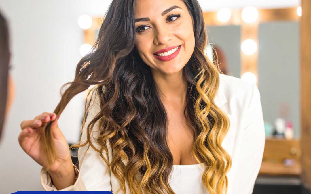 Lächelnde Frau mit glänzenden, gewellten Bonding Extensions betrachtet ihr Haar im Friseursalon – natürliches Licht, warmer Farbton, professioneller Look.
