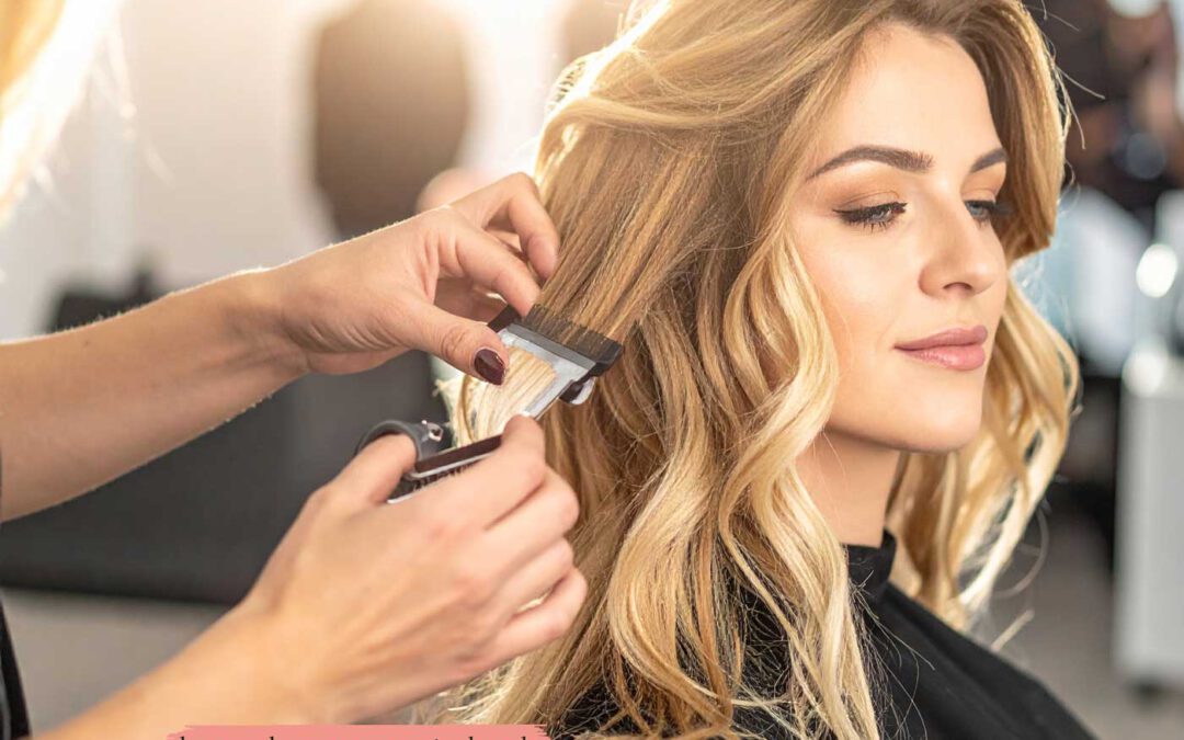 Friseurin befestigt Tape-In Extensions im Haar einer Kundin im Salon